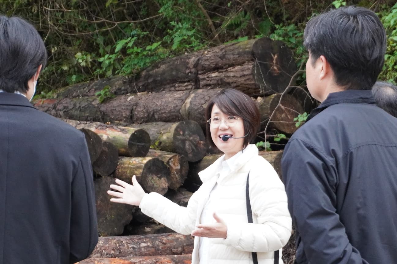 丸太の前で身振りを交えながら木材について説明している見学風景