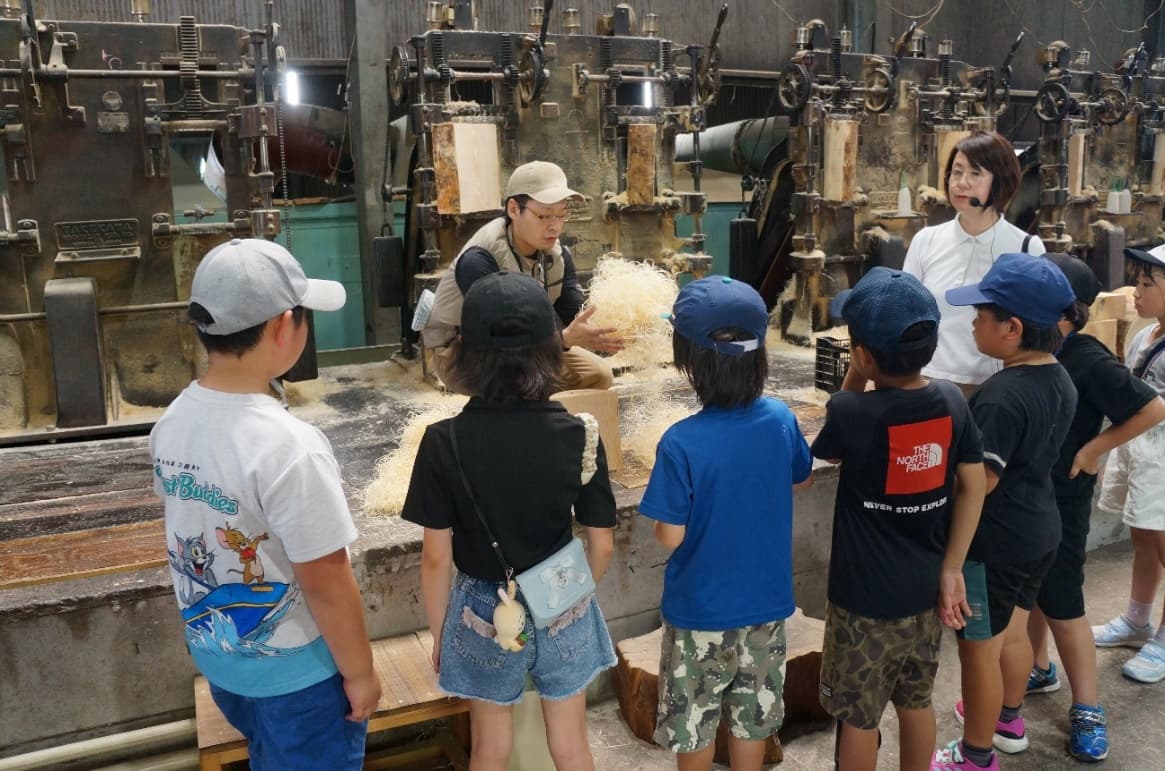 もくめん製造機の前で、子どもたちが原料を間近で見学している工場体験の様子