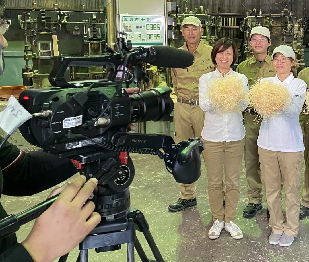 工場内で撮影取材が行われ、スタッフ達がもくめんを手に説明している様子